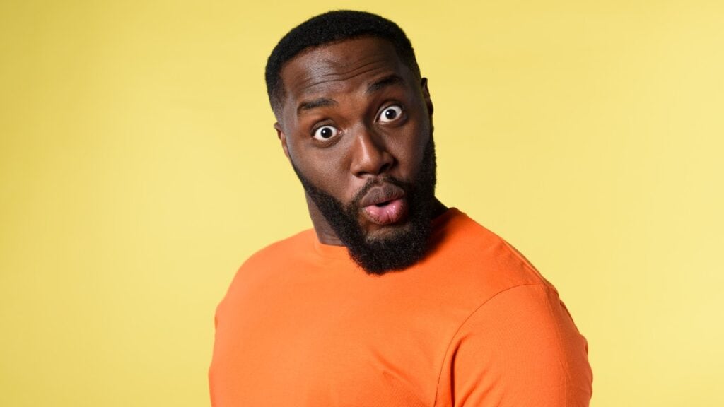 Vibrant portrait of a surprised African American man wearing an orange shirt against a yellow background, highlighting social media engagement and WOW factor.