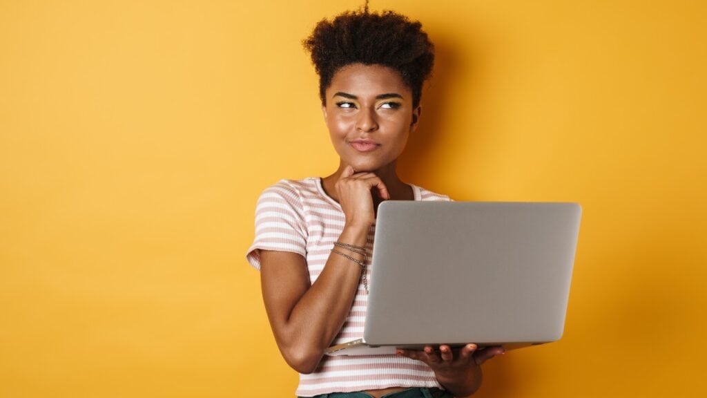 Vibrant woman using a laptop against a yellow background, representing social media marketing and digital engagement.